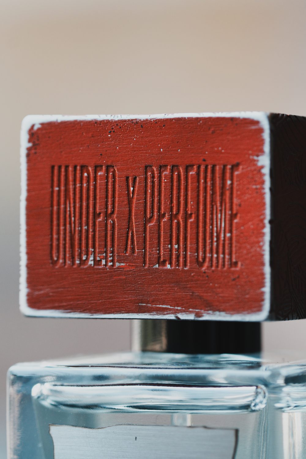 Close-up of the UNDER x PERFUME embossed cap above the glass bottle
